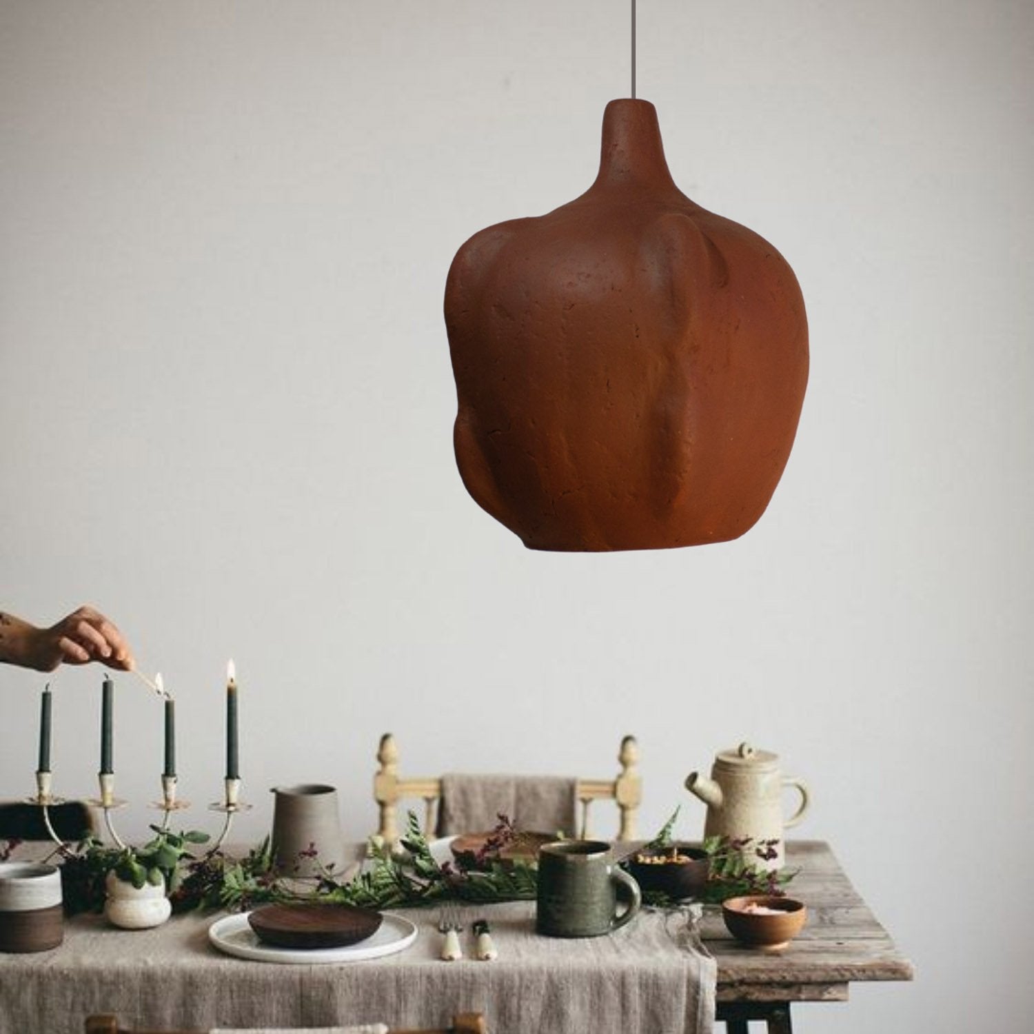 Dining table setting with a rustic lampshade hanging above, on a earthy red color, with a sculptural curvy shape made from papaer mache, 