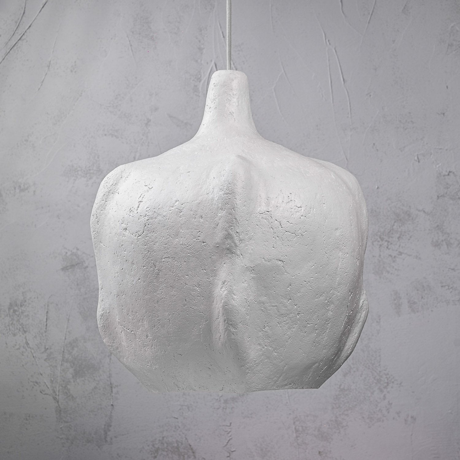 White textured pendant light against a gray concrete wall is a modern large ceiling lamp for kitchen island or living room made from paper mache that looks like ceramic 