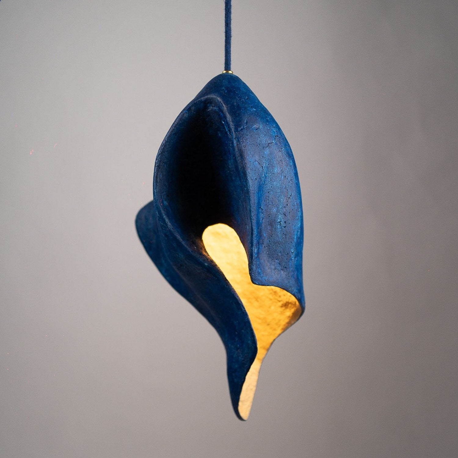Decorative hanging sculpture with blue and gold leaf design on a gray background, looks like a flame and is a pendant from paper mache