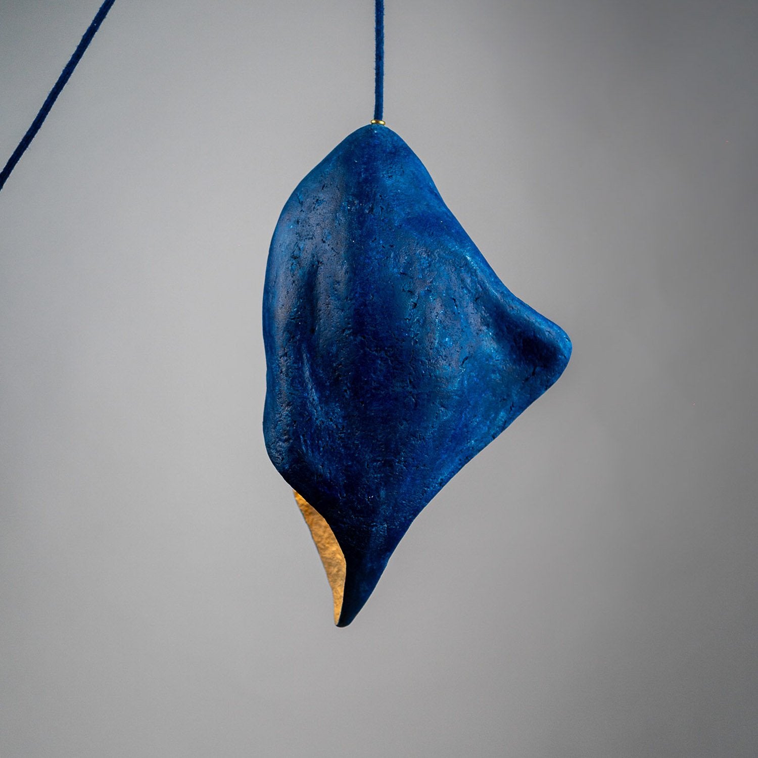 Blue hanging light object on a gray background ina flame shape. A pendant from paper mache 45 cm made by hand artisanal