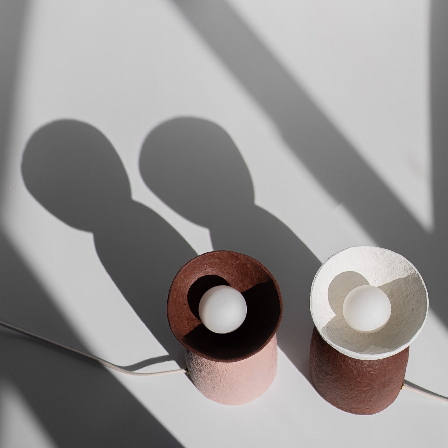 Two paper mache bedside table lamps with a white light bulb on a light gray background, with girl colors red, pink and white
