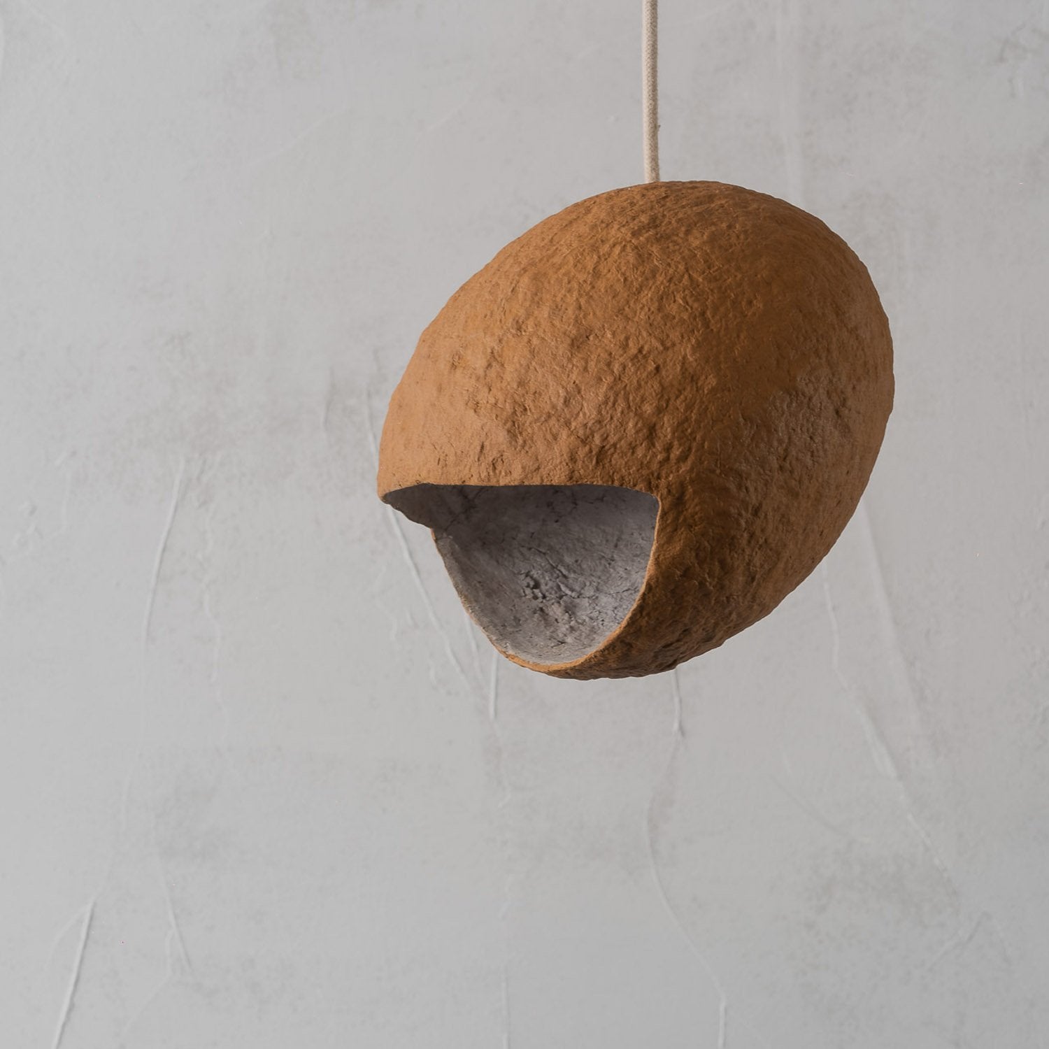 Coconut shell look pendant light hanging against a plain background on a golden terracotta orange color