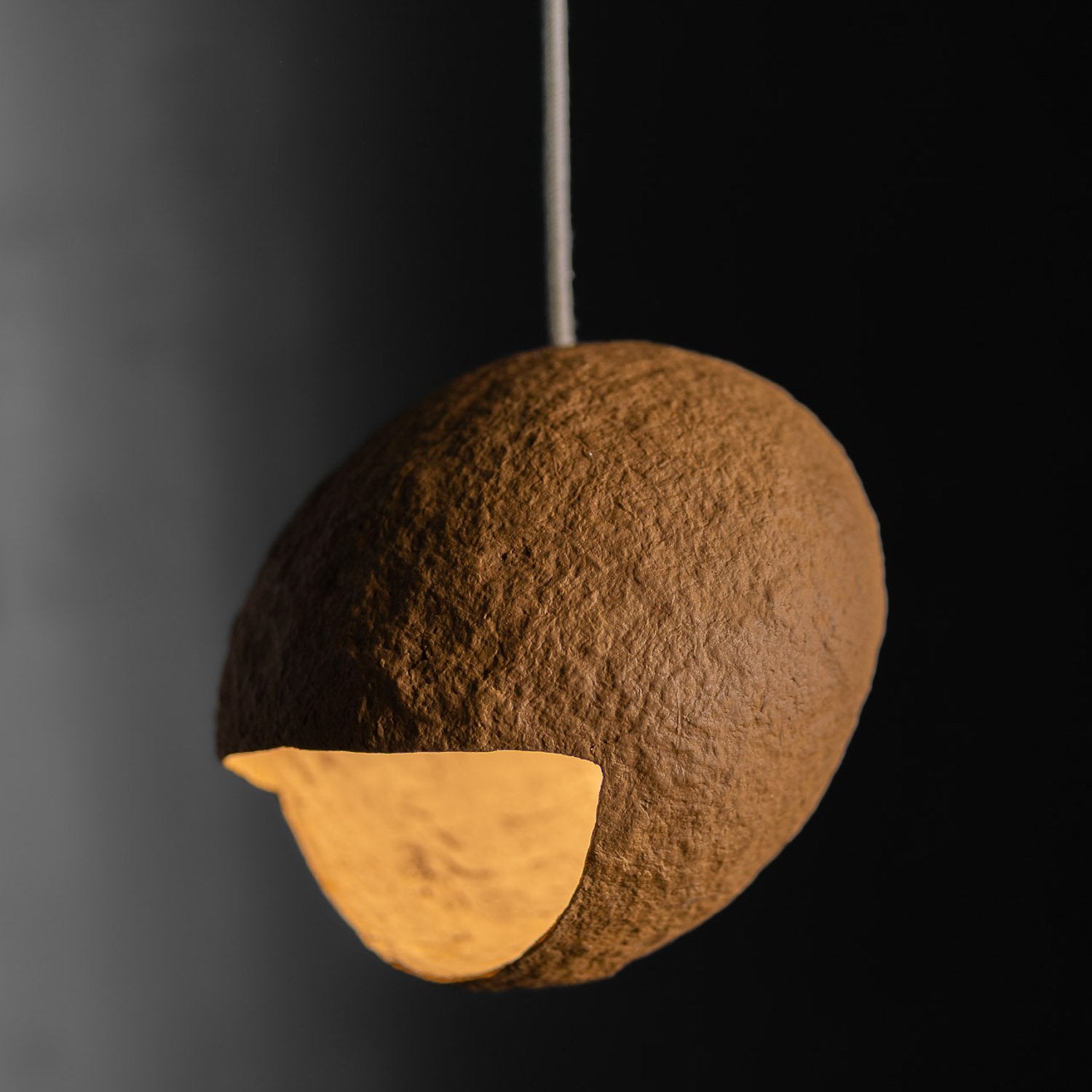 Spherical pendant light with textured brown surface and gold interior from paper mache on a black background
