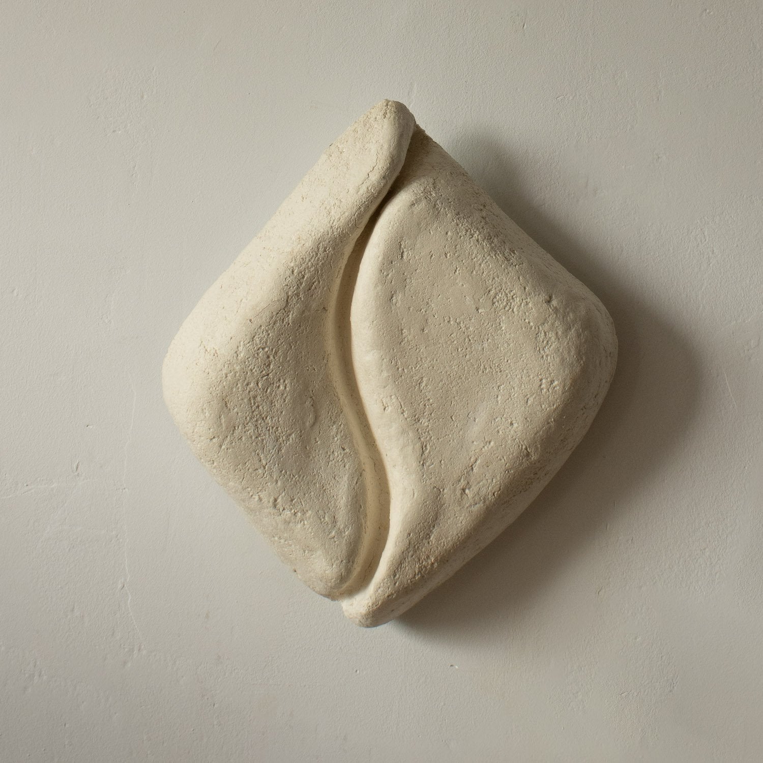 Beige paper mache wall art piece with light that looks like ceramic on a plain background