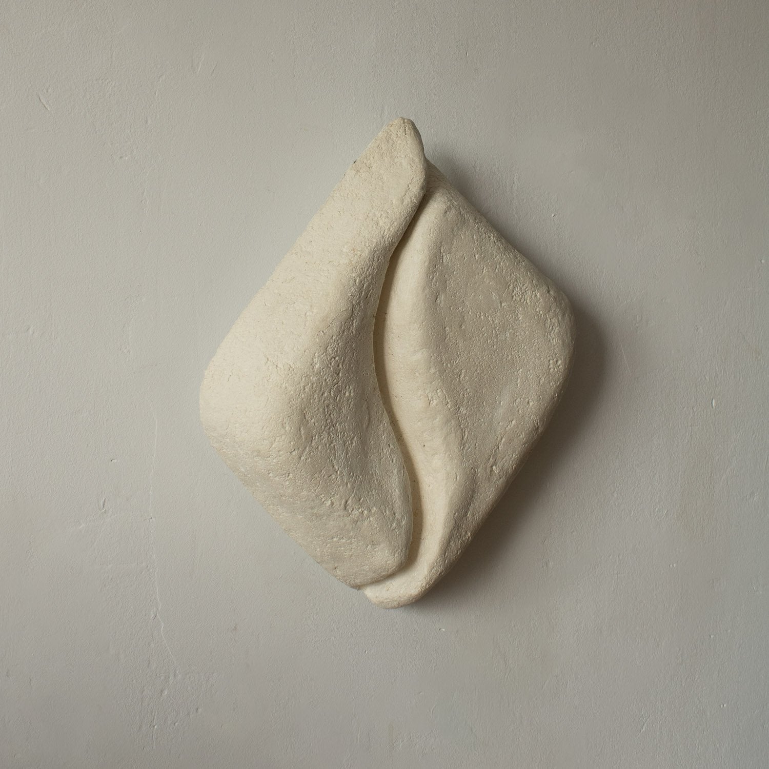 White paper mache wall lamp that is a sculptural art piece on a beige background