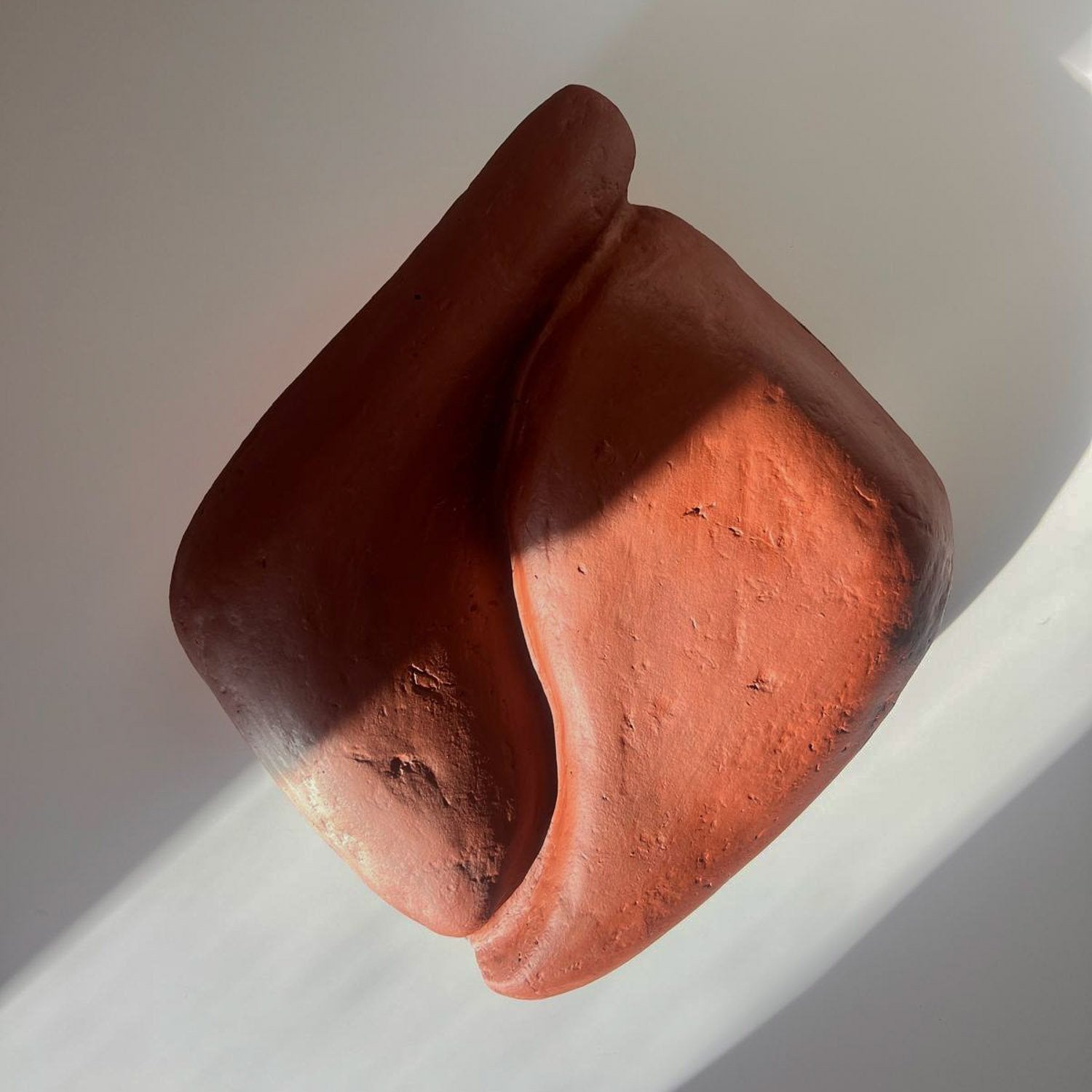 earthy red colored paper mache wall light with a sculptural curvy shape